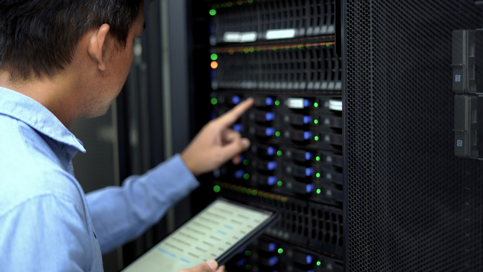 An IT professional in a blue shirt manages and monitors network servers in a data center, ensuring system stability and security.